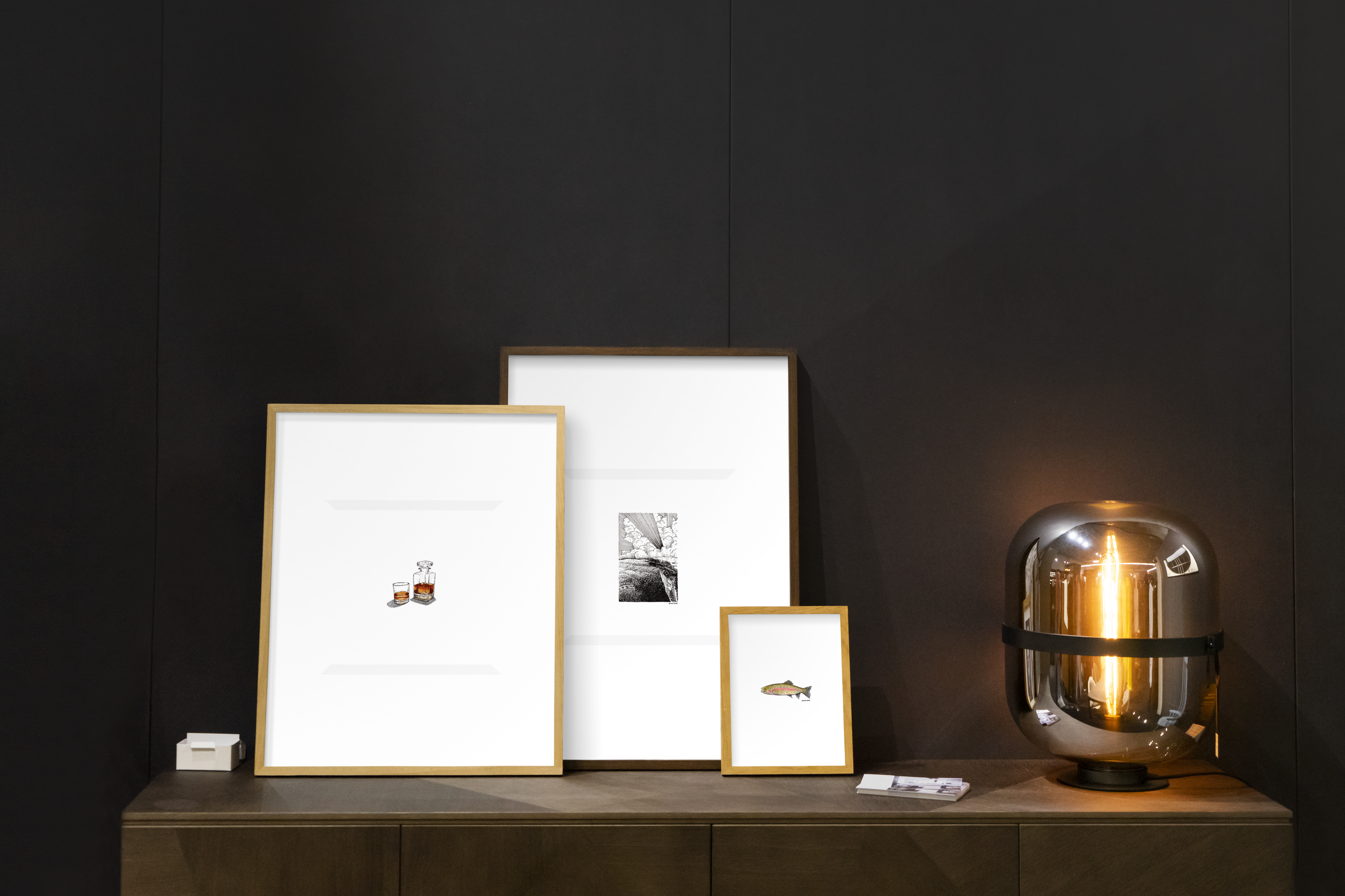 Three frames containing miniature artwork of a bourbon bottle, a rainbow trout, and a mountain sunset.